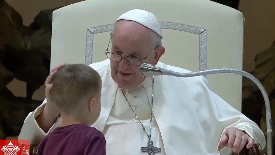 Papa Franscico acolhendo uma criança que veste uma blusa roxa